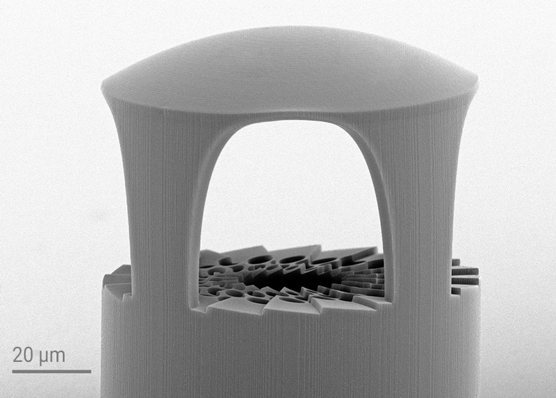 Close-up SEM image partially shows a 3D-printed fiber-based Bessel beam generator, displaying the photonic crystal design with a spiral phase plate and the microlens with supporting structures.